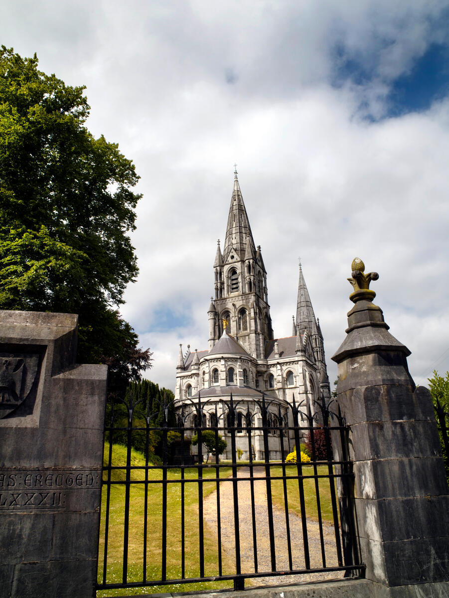 St Fin Barre&rsquo;s Cathedral seen through its entrance gates, with Gothic spires rising against a cloudy Cork sky.